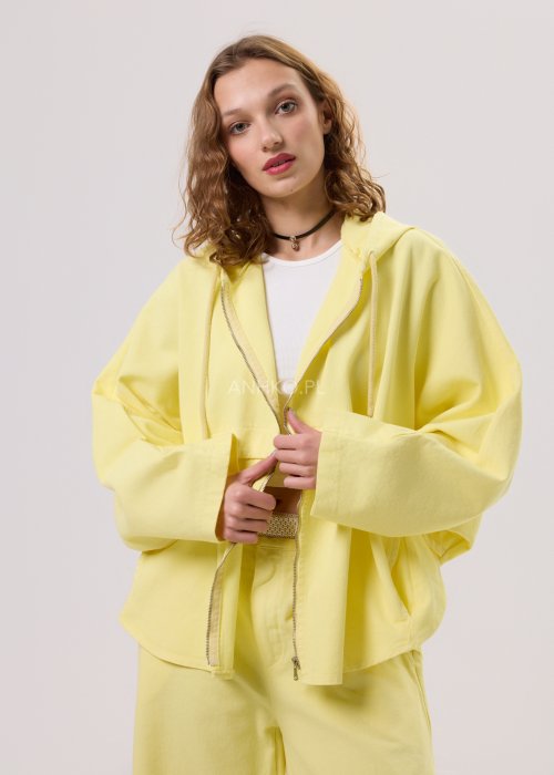 Żółta kurtka damska z kapturem zapinana na zamek, o luźnym kroju z szerokimi rękawami, w lekkim stylu casual.
