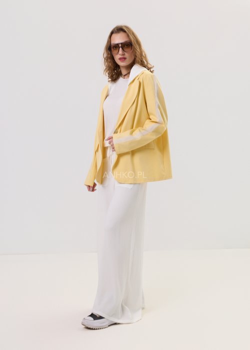 Żółta marynarka damska z kontrastowym kapturem i jasnymi lampasami na rękawach, zapinana na guziki, o luźnym kroju.
