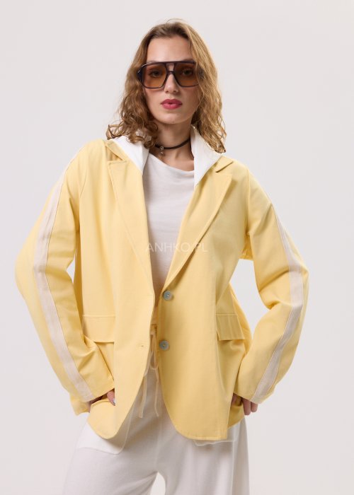 Żółta marynarka damska z kontrastowym kapturem i jasnymi lampasami na rękawach, zapinana na guziki, o luźnym kroju.