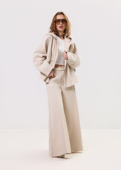 Beżowa kurtka damska z kapturem zapinana na zamek, o luźnym kroju z szerokimi rękawami i kieszeniami, w stylu casual.