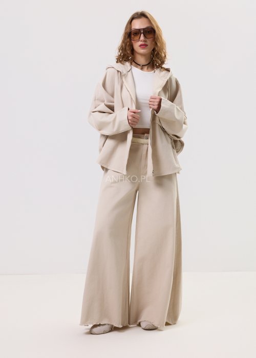 Beżowa kurtka damska z kapturem zapinana na zamek, o luźnym kroju z szerokimi rękawami i kieszeniami, w stylu casual.