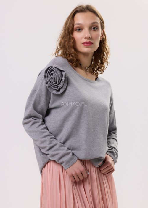 Szary damski sweter z długim rękawem i ozdobną różą na ramieniu, stylizowana z plisowaną różową spódnicą