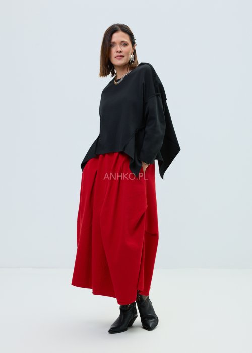 Czarna bluza oversize z szerokimi rękawami i asymetrycznym dołem, o luźnym, nowoczesnym kroju. Stylizacja z czerwoną spódnicą midi i botkami w wyrazistym, miejskim stylu.
