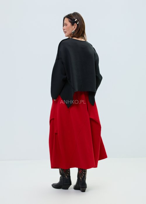 Czarna bluza oversize z szerokimi rękawami i asymetrycznym dołem, o luźnym, nowoczesnym kroju. Stylizacja z czerwoną spódnicą midi i botkami w wyrazistym, miejskim stylu.