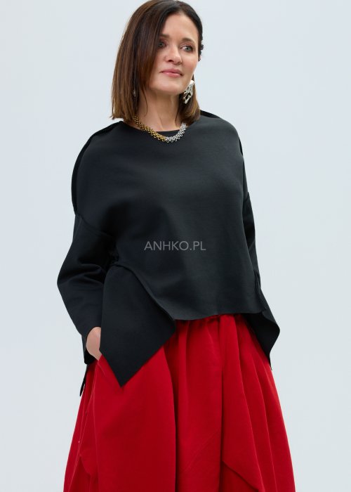 Czarna bluza oversize z szerokimi rękawami i asymetrycznym dołem, o luźnym, nowoczesnym kroju. Stylizacja z czerwoną spódnicą midi i botkami w wyrazistym, miejskim stylu.