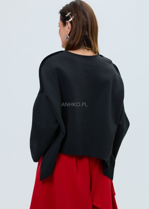 Czarna bluza oversize z szerokimi rękawami i asymetrycznym dołem, o luźnym, nowoczesnym kroju. Stylizacja z czerwoną spódnicą midi i botkami w wyrazistym, miejskim stylu.