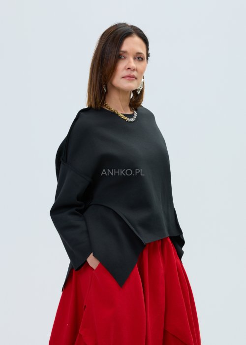 Czarna bluza oversize z szerokimi rękawami i asymetrycznym dołem, o luźnym, nowoczesnym kroju. Stylizacja z czerwoną spódnicą midi i botkami w wyrazistym, miejskim stylu.