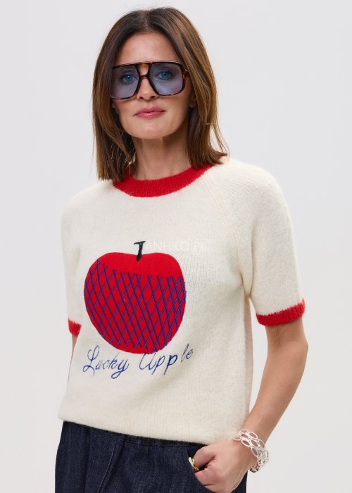 Kremowy sweter z czerwonymi mankietami i nadrukiem jabłka „Lucky Apple”, zestawiony z szerokimi jeansami i czerwonymi sandałami w modnej stylizacji.