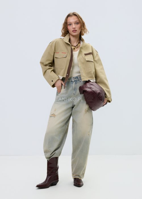 Krótka damska kurtka w kolorze camel z kieszeniami i ozdobnymi detalami, stylizowana z jasnymi jeansami.