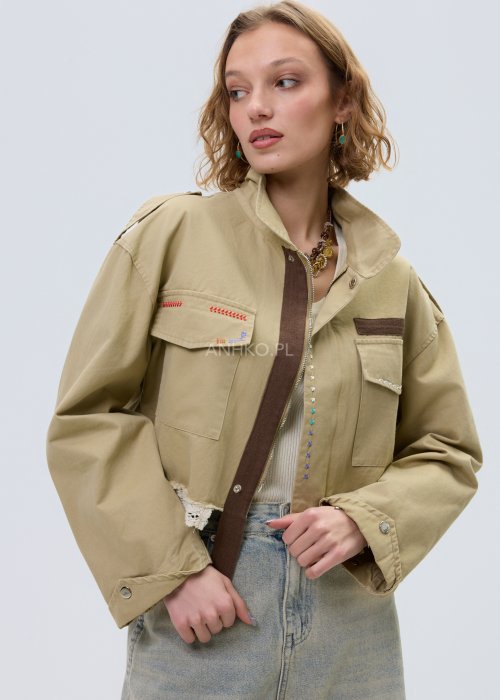 Krótka damska kurtka w kolorze camel z kieszeniami i ozdobnymi detalami, stylizowana z jasnymi jeansami.