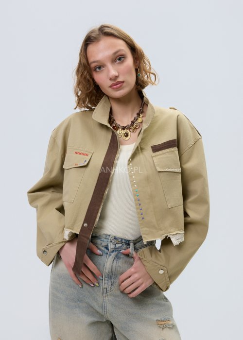 Krótka damska kurtka w kolorze camel z kieszeniami i ozdobnymi detalami, stylizowana z jasnymi jeansami.
