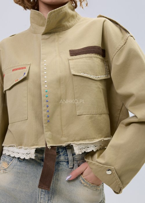 Krótka damska kurtka w kolorze camel z kieszeniami i ozdobnymi detalami, stylizowana z jasnymi jeansami.