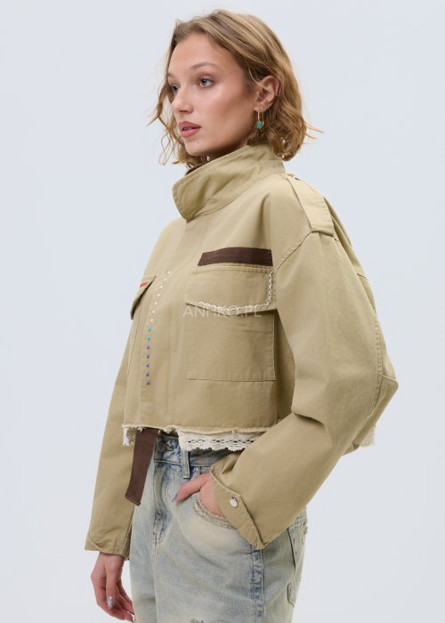 Krótka damska kurtka w kolorze camel z kieszeniami i ozdobnymi detalami, stylizowana z jasnymi jeansami.