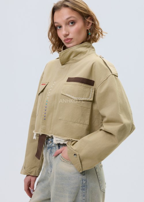 Krótka damska kurtka w kolorze camel z kieszeniami i ozdobnymi detalami, stylizowana z jasnymi jeansami.