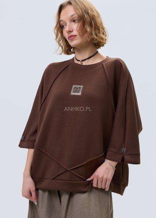 Brązowa damska bluza oversize z krótkim rękawem i zaokrąglonym dekoltem, model z ozdobną aplikacją na przodzie i dekoracyjnymi przeszyciami.