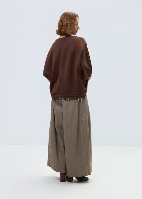 Brązowa damska bluza oversize z krótkim rękawem i zaokrąglonym dekoltem, model z ozdobną aplikacją na przodzie i dekoracyjnymi przeszyciami.