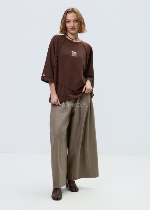 Brązowa damska bluza oversize z krótkim rękawem i zaokrąglonym dekoltem, model z ozdobną aplikacją na przodzie i dekoracyjnymi przeszyciami.