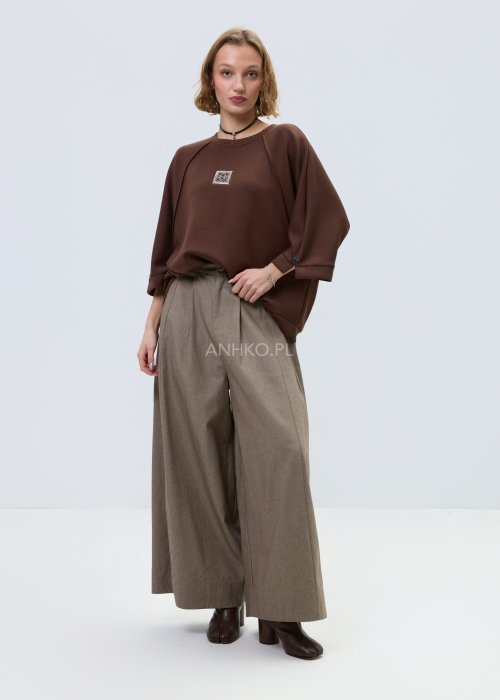 Brązowa damska bluza oversize z krótkim rękawem i zaokrąglonym dekoltem, model z ozdobną aplikacją na przodzie i dekoracyjnymi przeszyciami.