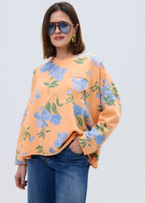 Damska bluza oversize w kolorze pomarańczowym z niebieskim kwiatowym wzorem, model z długim rękawem, zaokrąglonym dekoltem i kieszonką na piersi.