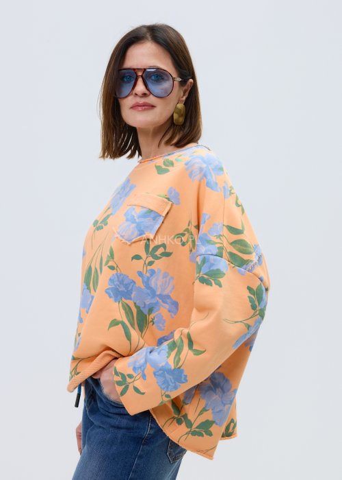 Damska bluza oversize w kolorze pomarańczowym z niebieskim kwiatowym wzorem, model z długim rękawem, zaokrąglonym dekoltem i kieszonką na piersi.