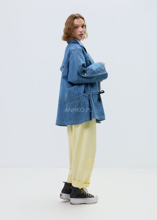Niebieska kurtka jeansowa oversize z szerokim kołnierzem i zapięciem na guziki, z regulacją w talii na troczki. Stylizacja z jasnym topem i spodniami w nowoczesnym, miejskim stylu.