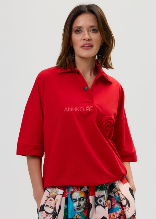 Czerwona bluzka damska oversize z dekoltem polo i zatrzaskami, z szerokimi rękawami, stylizowana ze wzorzystą spódnicą.