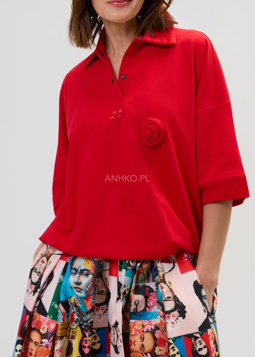 Czerwona bluzka damska oversize z dekoltem polo i zatrzaskami, z szerokimi rękawami, stylizowana ze wzorzystą spódnicą.