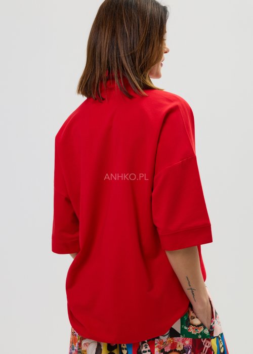 Czerwona bluzka damska oversize z dekoltem polo i zatrzaskami, z szerokimi rękawami, stylizowana ze wzorzystą spódnicą.