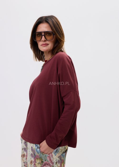 Luźna bordowa bluzka damska o oversize’owym kroju, z obniżoną linią ramion i długim rękawem.