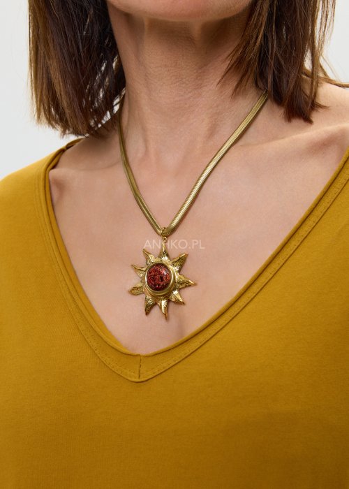 Złoty naszyjnik damski z ozdobną zawieszką w kształcie słońca z czerwonym kamieniem, na eleganckim łańcuszku.