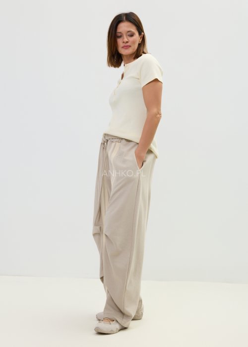 Spodnie damskie beżowe z luźnym krojem, szeroką nogawką i ozdobnymi paskami po bokach.
