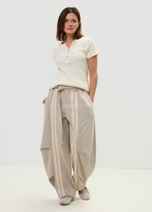 Spodnie damskie beżowe z luźnym krojem, szeroką nogawką i ozdobnymi paskami po bokach.