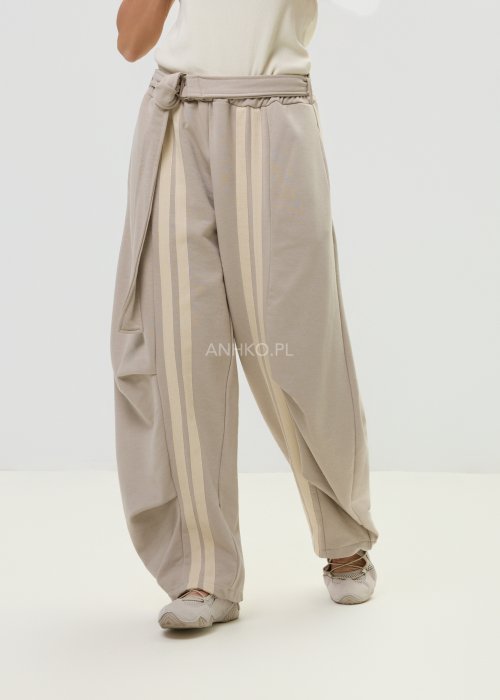 Spodnie damskie beżowe z luźnym krojem, szeroką nogawką i ozdobnymi paskami po bokach.