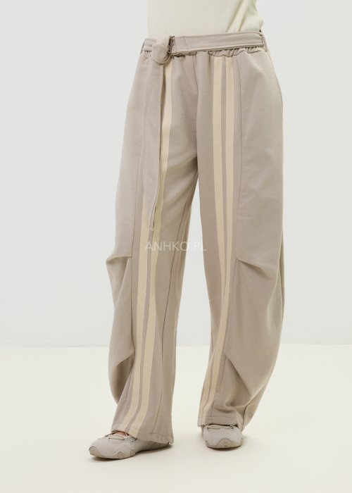 Spodnie damskie beżowe z luźnym krojem, szeroką nogawką i ozdobnymi paskami po bokach.