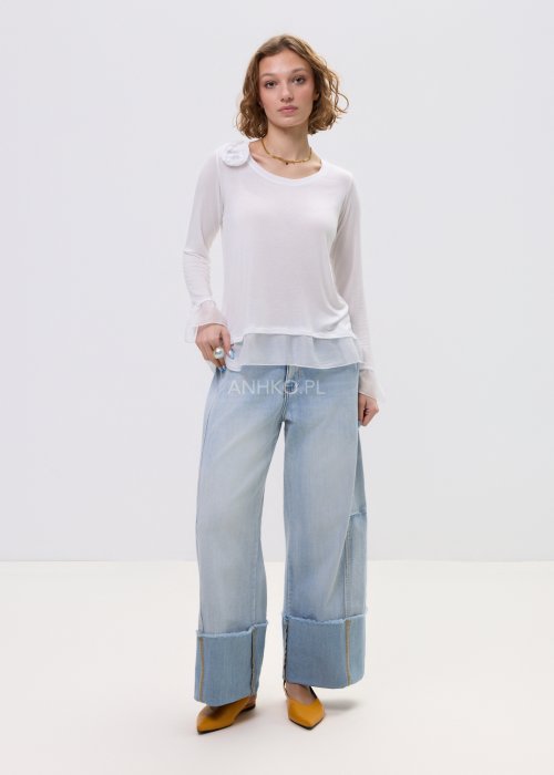 Biała bluzka damska z długim rękawem i delikatną falbaną na dole oraz przy mankietach, z ozdobnym kwiatem przy dekolcie.