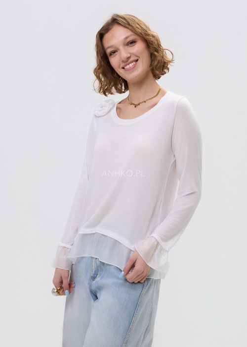 Biała bluzka damska z długim rękawem i delikatną falbaną na dole oraz przy mankietach, z ozdobnym kwiatem przy dekolcie.