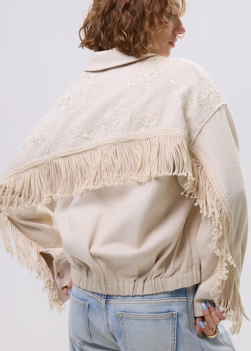 Beżowa kurtka damska z frędzlami i haftowanymi zdobieniami, zapinana na zamek, z kołnierzem i luźnym fasonem.