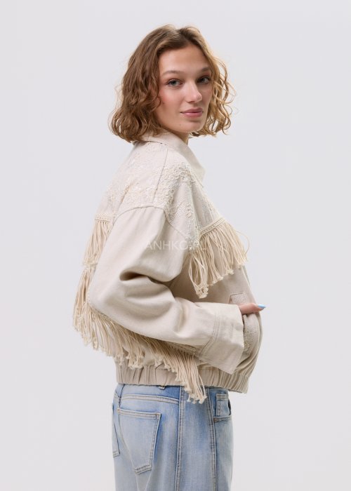 Beżowa kurtka damska z frędzlami i haftowanymi zdobieniami, zapinana na zamek, z kołnierzem i luźnym fasonem.