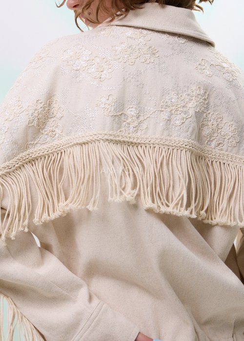 Beżowa kurtka damska z frędzlami i haftowanymi zdobieniami, zapinana na zamek, z kołnierzem i luźnym fasonem.