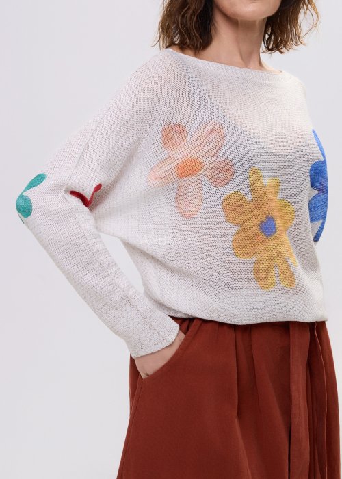 Kremowy sweter damski o luźnym kroju z kolorowym motywem kwiatów, z szerokim dekoltem i długim rękawem, stylizowany ze spódnicą maxi.