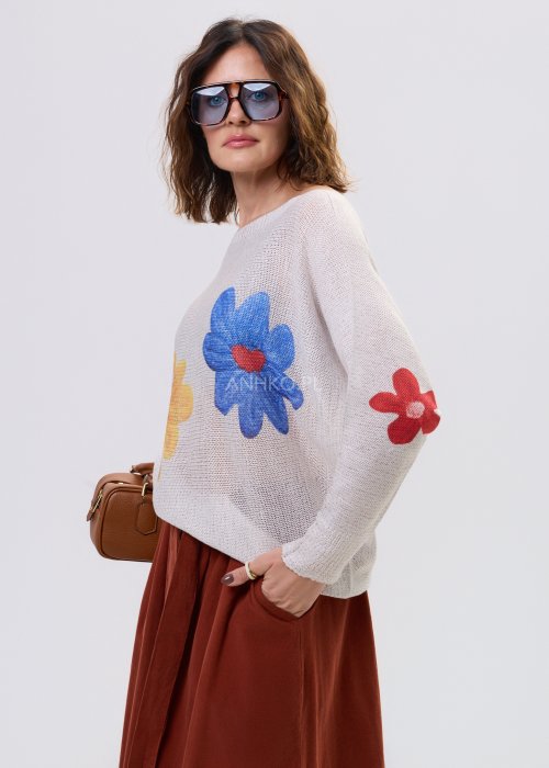 Kremowy sweter damski o luźnym kroju z kolorowym motywem kwiatów, z szerokim dekoltem i długim rękawem, stylizowany ze spódnicą maxi.