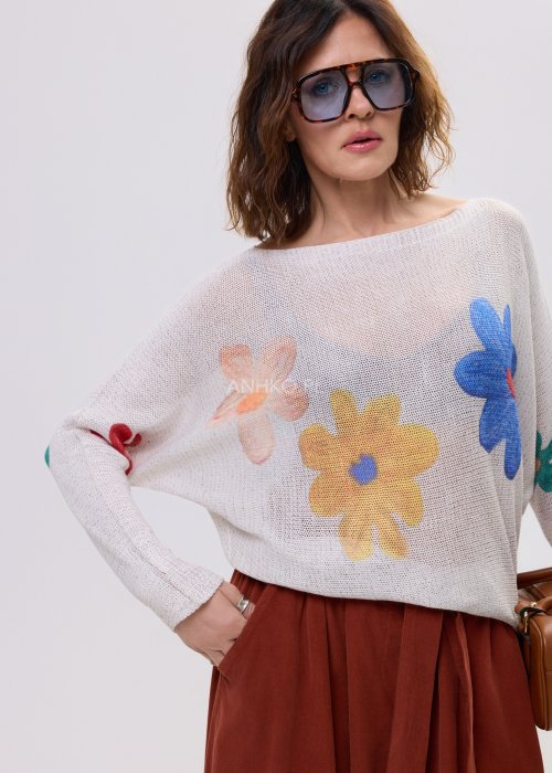 Kremowy sweter damski o luźnym kroju z kolorowym motywem kwiatów, z szerokim dekoltem i długim rękawem, stylizowany ze spódnicą maxi.