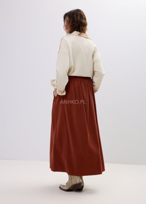 Koszula damska beżowa z haftowanym wzorem roślinnym w odcieniach karmelu, zapinana na guziki, z szerokim rękawem, stylizowana ze spódnicą midi.