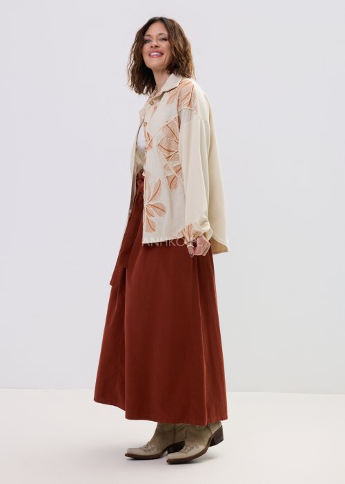 Koszula damska beżowa z haftowanym wzorem roślinnym w odcieniach karmelu, zapinana na guziki, z szerokim rękawem, stylizowana ze spódnicą midi.