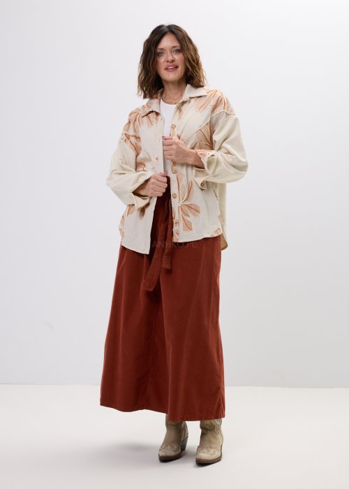 Koszula damska beżowa z haftowanym wzorem roślinnym w odcieniach karmelu, zapinana na guziki, z szerokim rękawem, stylizowana ze spódnicą midi.