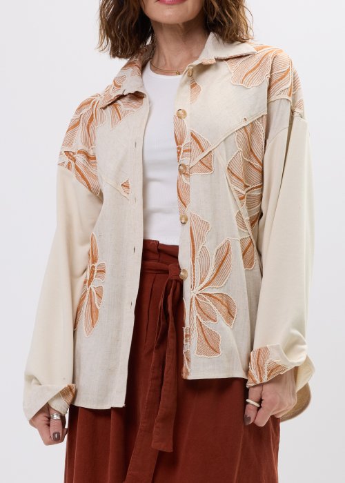 Koszula damska beżowa z haftowanym wzorem roślinnym w odcieniach karmelu, zapinana na guziki, z szerokim rękawem, stylizowana ze spódnicą midi.