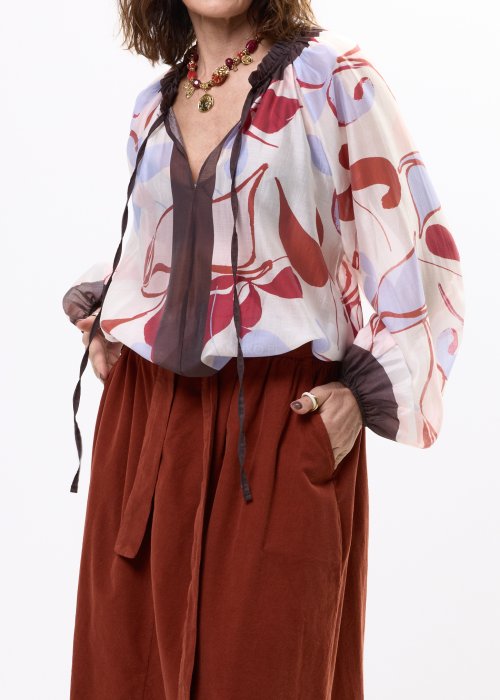 Bluzka damska z lekkiej, półtransparentnej tkaniny z abstrakcyjnym wzorem w odcieniach kremowym i czerwieni, z wiązaniem przy dekolcie i długimi rękawami.