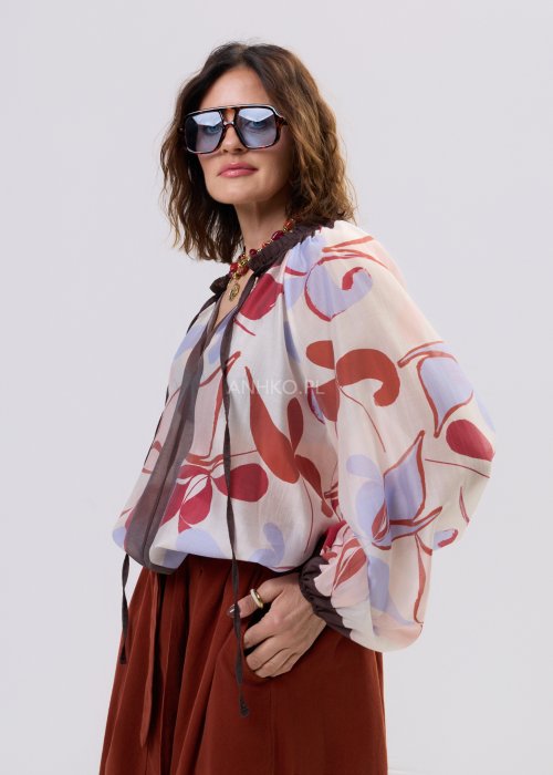Bluzka damska z lekkiej, półtransparentnej tkaniny z abstrakcyjnym wzorem w odcieniach kremowym i czerwieni, z wiązaniem przy dekolcie i długimi rękawami.