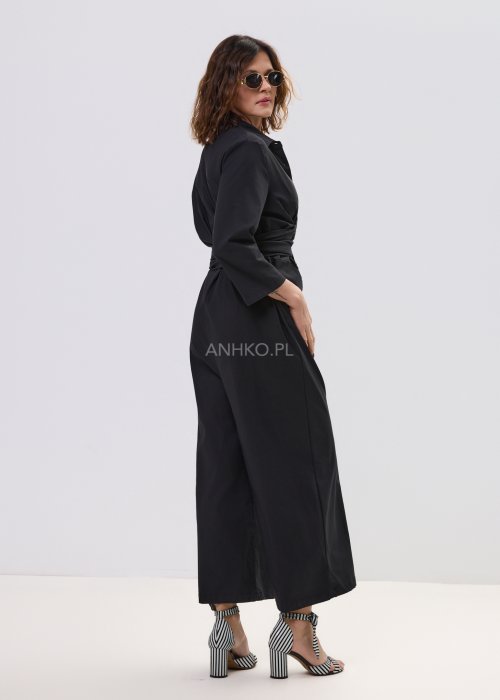 Czarny kombinezon damski z kopertową górą i paskiem w talii, z długim rękawem i szerokimi nogawkami, stylizowany z sandałami na obcasie.