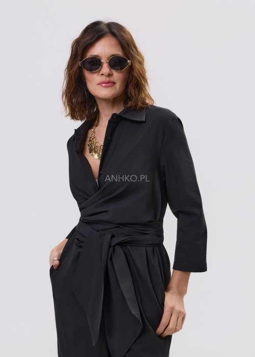 Czarny kombinezon damski z kopertową górą i paskiem w talii, z długim rękawem i szerokimi nogawkami, stylizowany z sandałami na obcasie.